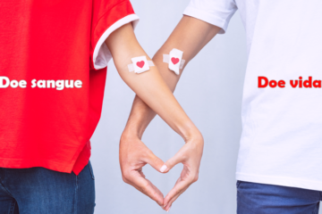 Imagem de uma mulher com camiseta vermelha e um hmem com camiseta brancos, ambos com os braços entrelaçados, formando com as mãos um coração e tendo no braço uma gaze com um coração