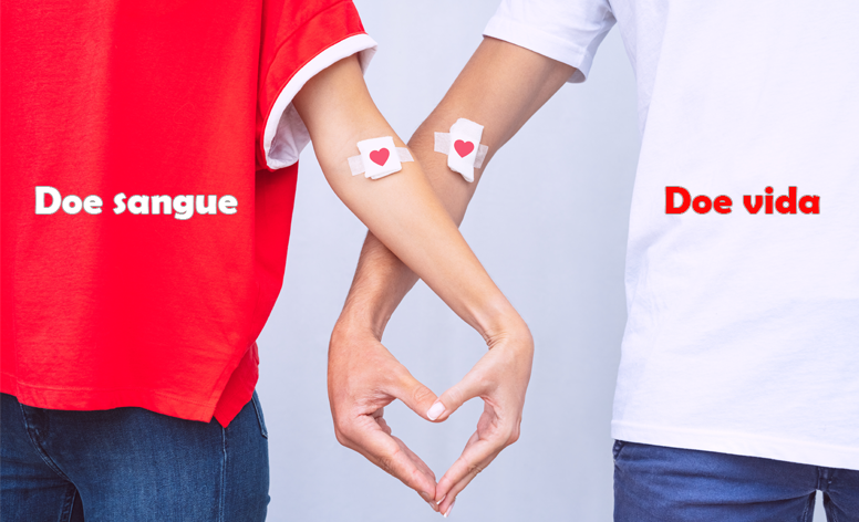 Imagem de uma mulher com camiseta vermelha e um hmem com camiseta brancos, ambos com os braços entrelaçados, formando com as mãos um coração e tendo no braço uma gaze com um coração