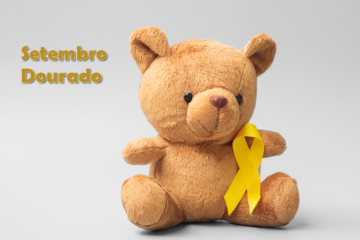 Foto de um ursinho de pelúcia marrom com um laço dourado em seu peito representando o setembro dourado, mês de conscientização do câncer infantojuvenil. Ao lado do ursinho o nome Setembro Dourado